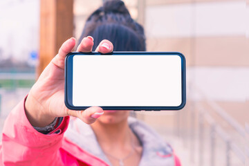 Girl in a pink jacket holds a smartphone mockup with white screen in hands. Mock-up Technology.