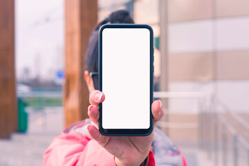 Girl in a pink jacket holds a smartphone mockup with white screen in hands. Mock-up Technology.