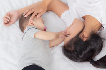 Fototapeta na wymiar Young asian mother touch head of little baby girl with tender on bed in the bedroom, mom love newborn and care, woman with expression with child together, parent and daughter, family concept.