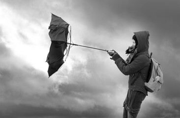 Eine Frau versucht bei starkem Wind einen Regenschirm festzuhalten. Im Hintergrund sind drohende Gewitterwolken zu sehen.