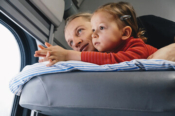 Father with child travalling in the train, having fun enjoying scene through window while riding on railroad togather in sleeping car