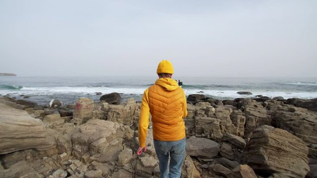 Father is filming his daughter who is jumping and walking on big stones on the seaside. Ocean is on the background