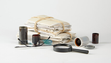 A stack of old photographs, negatives, glasses and a magnifier on a white background.