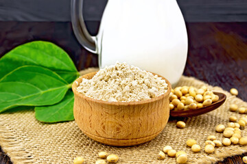 Flour soy in bowl with milk and soybeans on dark board