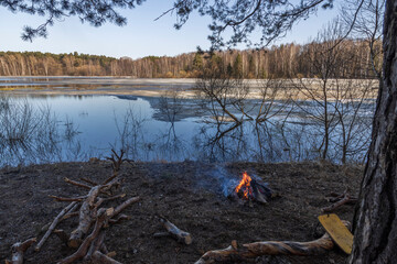 A cozy bonfire on the bank of the river in early spring. In the spring, a small warm fire. Lonely fire on the river bank, tourists rest.
