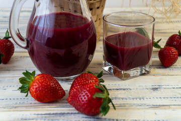 Strawberry in basket and on table on wooden background, strawberry juice in jug