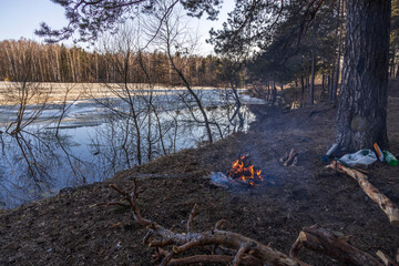 A cozy bonfire on the bank of the river in early spring. In the spring, a small warm fire. Lonely fire on the river bank, tourists rest.