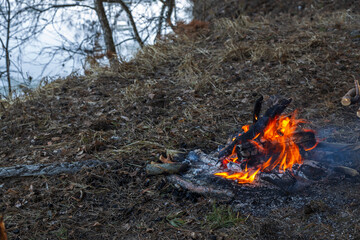 A cozy bonfire on the bank of the river in early spring. In the spring, a small warm fire. Lonely fire on the river bank, tourists rest.