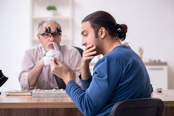 Young man visiting old male jeweler