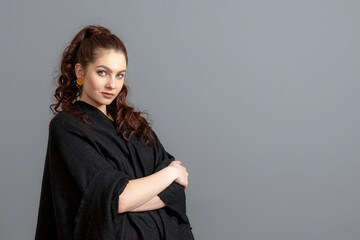 portrait of charming curly-haired woman in a black cloak isolated on a gray background