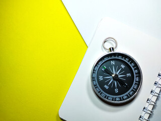 Selective focus of compass and notebook on yellow and white background with copy space.