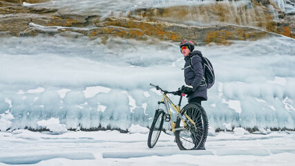 Man is riding bicycle near ice grotto. Rock with ice caves icicl