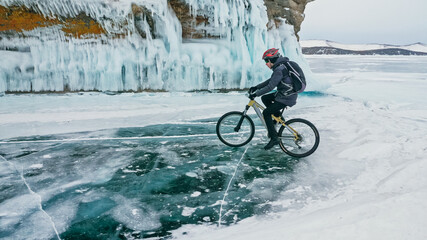 Man is riding bicycle near ice grotto. Rock with ice caves icicl