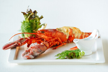 Cooked lobster with grilled cheese, lettuce leaves, dill or fennel, lemon and oily sauce in gravy boat. Fancy cuisine food. Side view
