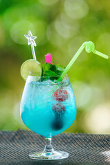 Vertical picture of blue cocktail with lime, cherries and mint in cognac glass on background of green bokeh 