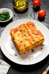 Portion of ground beef lasagne topped with melted cheese and garnished with fresh parsley served on a gray plate .	