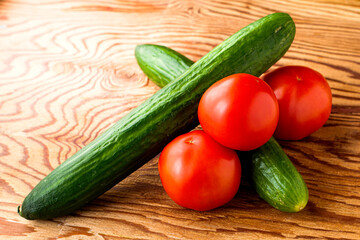 two cucumbers and three tomatoes on a wooden surface