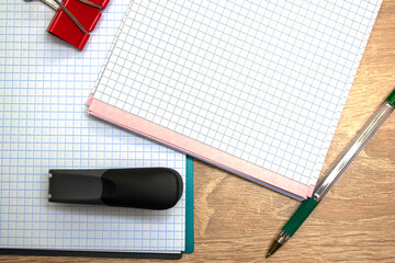two open notepads a fountain pen a stapler and a stationery clip on the table