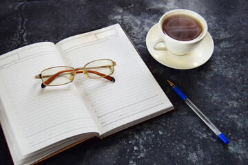 Remote online work, business concept diary with glasses and pen, hot cup of tea
