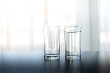 A glass cup of water on the table(desk), day light in the morning.