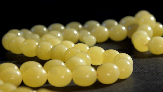 Crafted white matt amber beads on rosary sample lying on grey support at exhibition macro. Concept accessory production