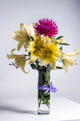 A bouquet of lilies and dahlias in a vase stands on a white table, isolated against an empty background