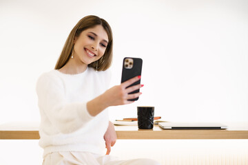 Woman with candid smile chatting by phone and enjoying coffee break in cafe . Wearing casual white sweater and pants.