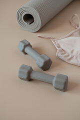 Aesthetic creative concept. Yoga, fitness, workout training equipment on neutral beige background. Dumbbells, top, mat. Sport influencer blog