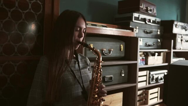 Beautiful young woman with alto saxophone standing in a jazz club and play the keys of the jazz saxophone dressed with a grey dress in a calm and happy mood