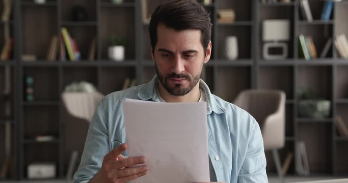 Handsome young caucasian man looking through paper correspondence at home office, reading letter with amazing news, celebrating getting bank loan approval or dream job offer, success good luck concept