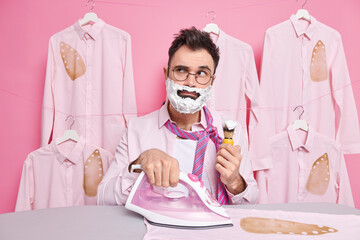 Serious man shaves and irons clothes at home concentrated away burned shirt as being deep in...