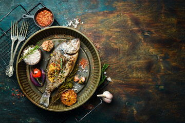 Baked dorado fish with asparagus and vegetables in a metal tray. Free copy space. On a black stone...