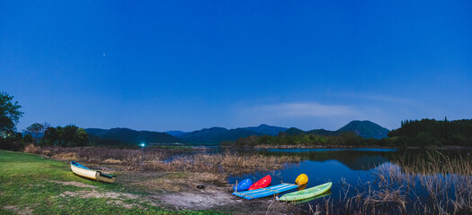 Panorama night view of mountain lake with kayaks floating on the lakeside.