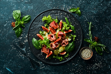 Green salad with prosciutto, cucumber and fig on a black stone plate. Food. Top view. Free space for your text.