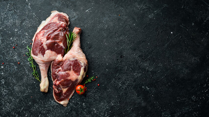 Poultry meat. Fresh raw duck thigh with rosemary and spices. On a black stone background. Top view. - obrazy, fototapety, plakaty