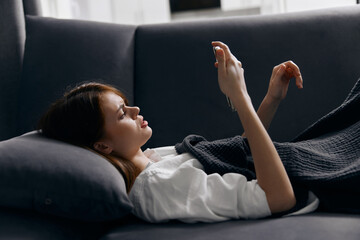 a woman in a comfortable room lies on a gray sofa with a mobile phone in her hand