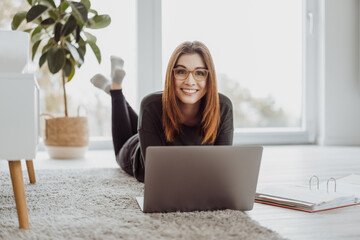 Happy casual young woman lying on the floor with her laptop