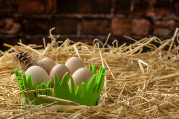Obraz premium Easter eggs in a basket on straw against a brick wall background. Copy space.