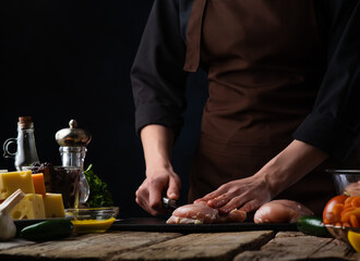 Chef cuts chicken fillet on the background of food.Cooking meat, and recipes with chicken.Culinary recipes and cooking.Concept of a book of recipes and menus for restaurants, hotels and cafes