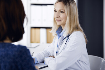 Friendly female doctor and patient woman discussing current health examination while sitting in...