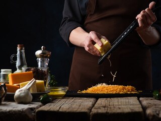 Chef prepares grated cheese for making Italian pizza, on the background of ingredients. Freezing in motion. Recipes, photos for illustrating cookbooks and recipes