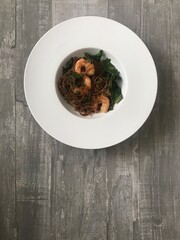 Closeup image of a bowl of honey sesame prawns served with rice noodles against a wooden background 