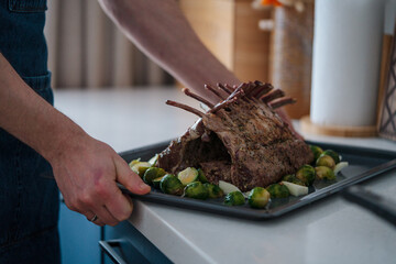 Roasted rack of lamb on a tray in the hands of the chef.