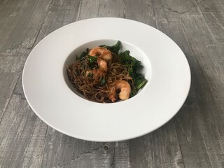 Closeup image of a bowl of honey sesame prawns against a wooden background 