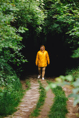 traveler man in yellow raincoat hiking by rainy forest