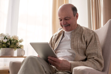 Senior man websurfing on internet with digital tablet sitting at home