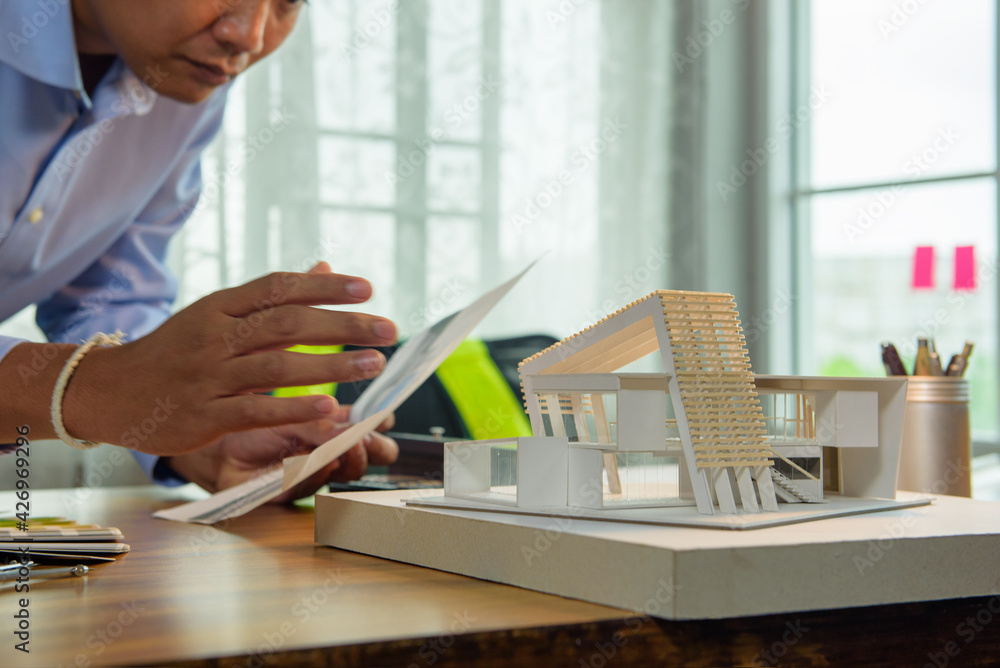 Poster architect-designer working with model of modern box house while thinking about concept of building a