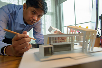 Architect-designer working with model of modern box house while thinking about concept of building and construction project before startup in the future.