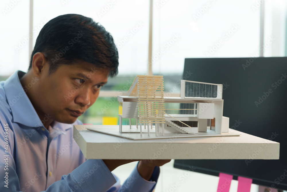 Poster architect-designer holding model of modern box house while thinking about concept of building and co