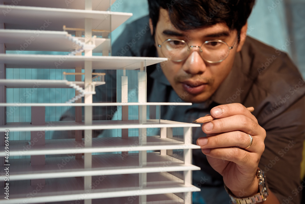 Poster architect-designer working at night with model of hight building while thinking about concept of bui